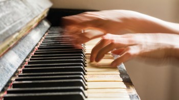 Hands playing a piano, with the keys in focus and the pianist's hands blurred.
