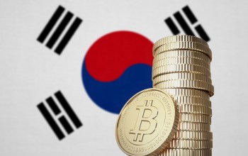 A stack of gold coins with a Bitcoin symbol in front of the South Korean flag.