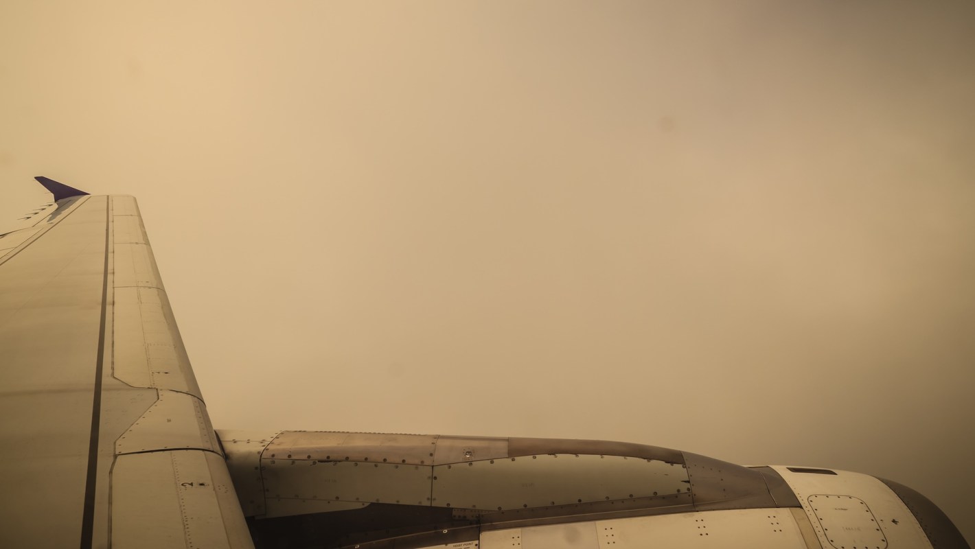 An airplane wing extends into a hazy, beige sky, creating a serene yet mysterious atmosphere.