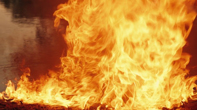 Bright flames dancing against a dark background near a reflective surface.