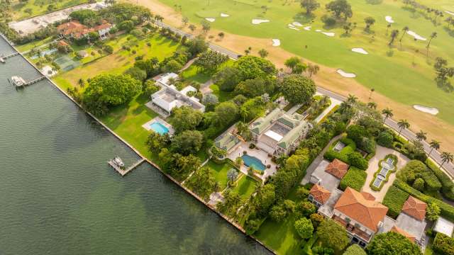 An aerial view of luxurious waterfront homes, landscaped gardens, and a golf course in the background.
