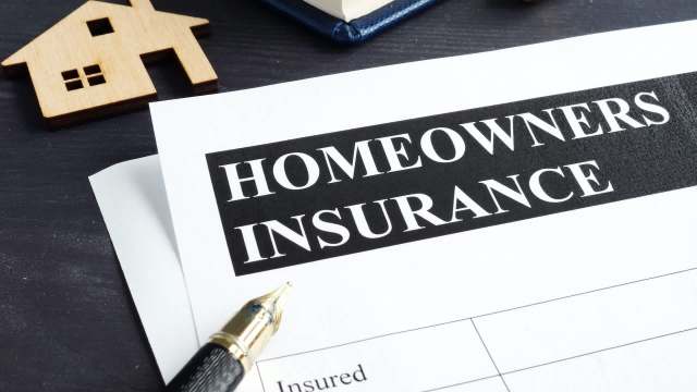 A homeowners insurance document featuring a pen and a wooden house model.