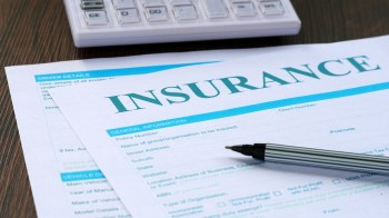 A close-up of an insurance form with a pen and a calculator on a wooden surface.