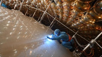 A technician inspects a large reflective surface in a laboratory filled with illuminated spheres above.