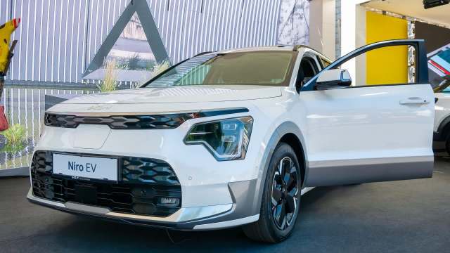A white Kia Niro EV parked with its driver's side door open, showcased at an exhibit.