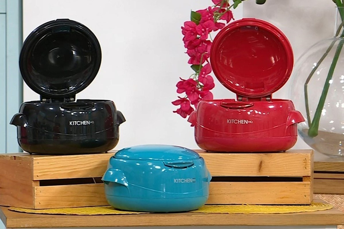 Three colorful kitchen appliances in black, red, and blue displayed on wooden crates with pink flowers in the background.