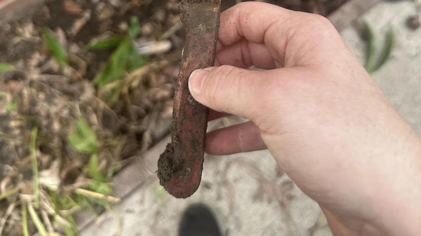 A hand holding a weathered, dirt-covered tool.