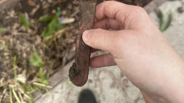 A hand holding a weathered, dirt-covered tool.