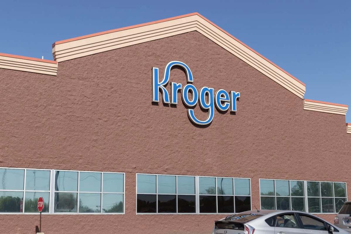 A Kroger grocery store exterior featuring its logo on a brown wall and large windows.