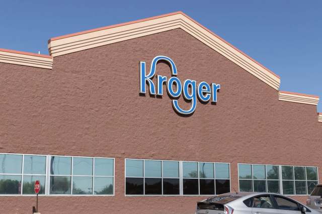 A Kroger grocery store exterior featuring its logo on a brown wall and large windows.