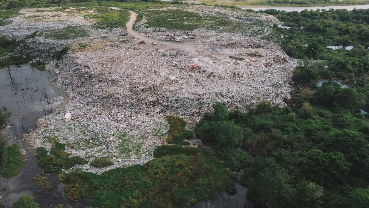 Aerial view of a large rubbish dump surrounded by green vegetation and stagnant water.