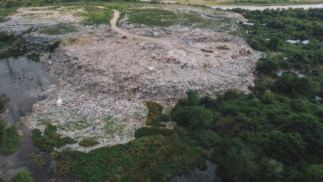 Aerial view of a large rubbish dump surrounded by green vegetation and stagnant water.