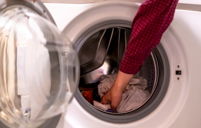 A person reaches into a washing machine to retrieve clothes.