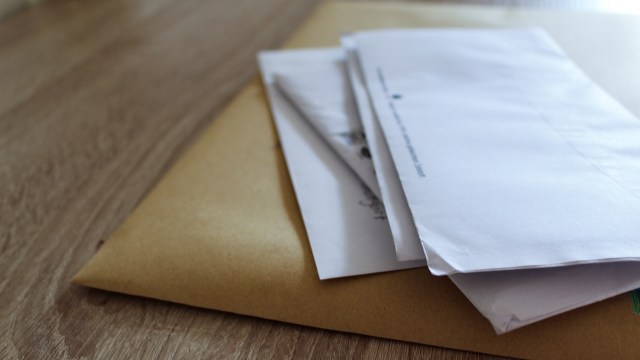 A stack of white envelopes atop a brown envelope on a wooden surface.
