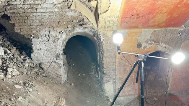 An underground space showing a dark archway, rubble, and bright lights on tripods illuminating the area.