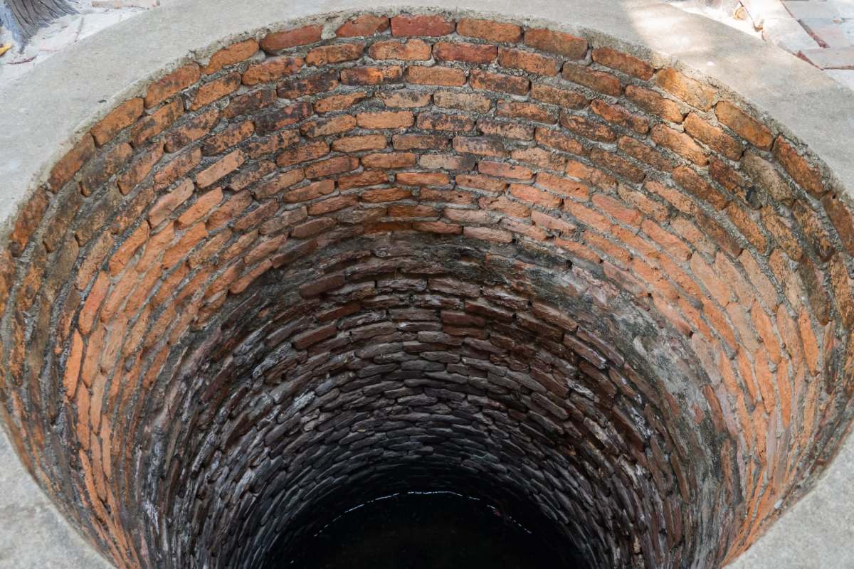 A close-up view of a cylindrical, brick-lined well with water at the bottom.