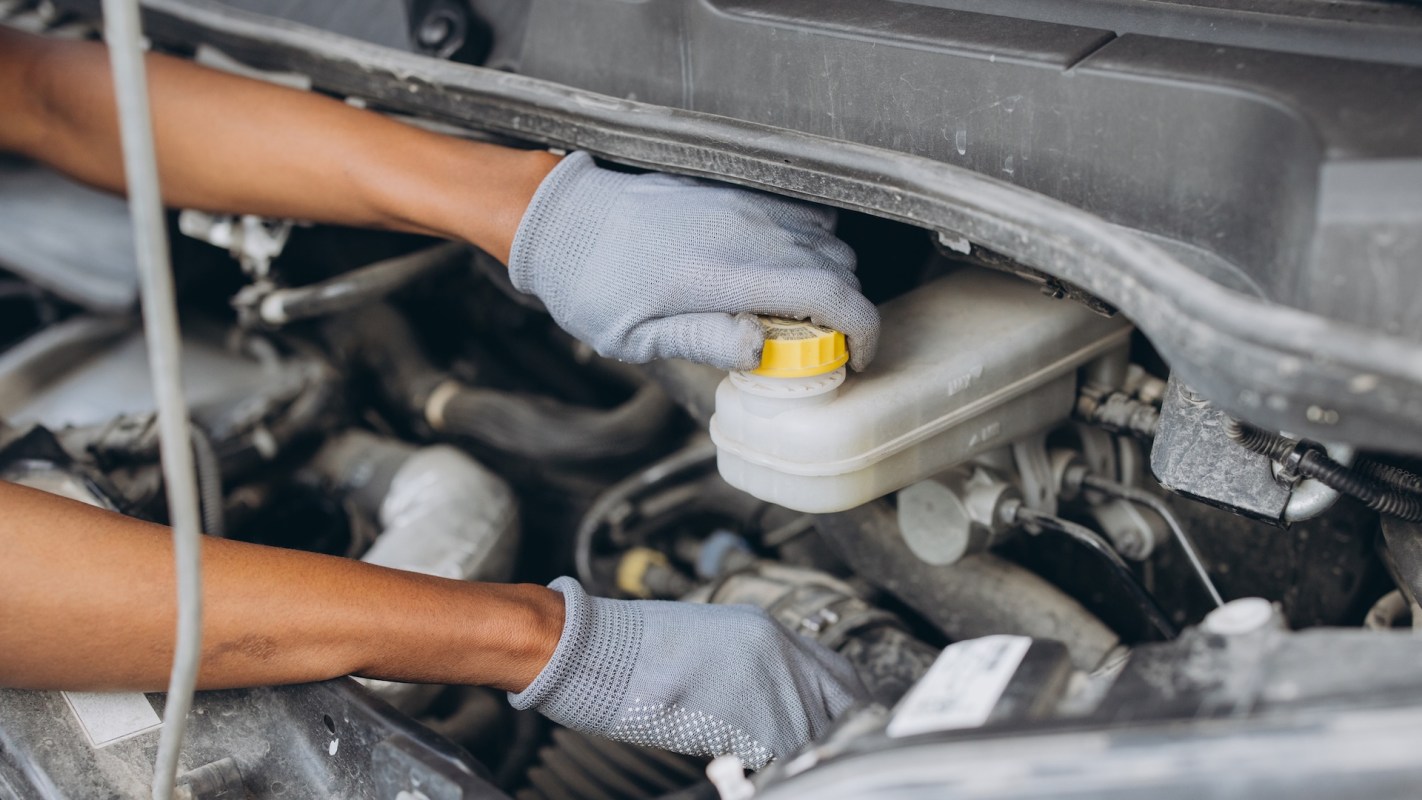 A person wearing gloves opens the coolant reservoir cap under a car hood.