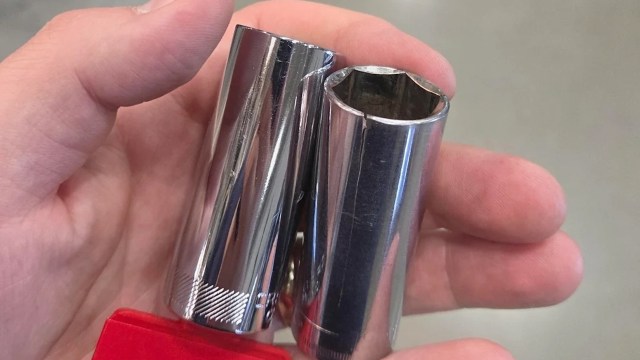 A person holds two shiny metal socket wrenches in their hand.