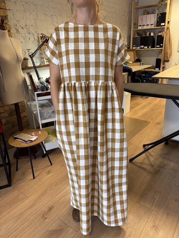 A person holds a red and white checkered fabric while standing next to neatly stacked patterned fabrics in a store.