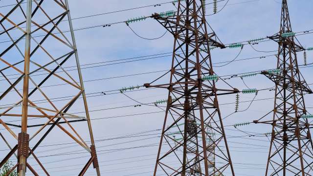 High-voltage power lines supported by metal towers against a cloudy sky.