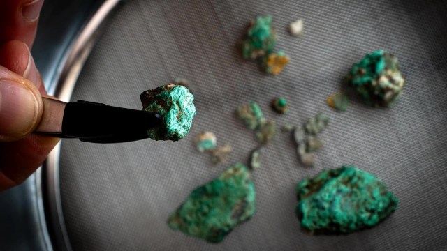 A hand holding a green mineral specimen with several similar pieces scattered in the background.