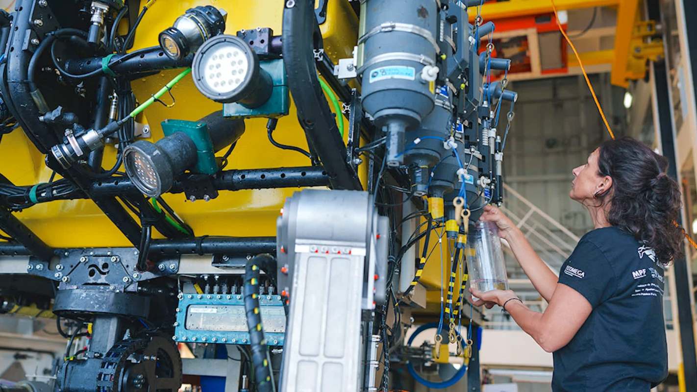 A woman inspects equipment on a yellow underwater vehicle in a technical workshop.