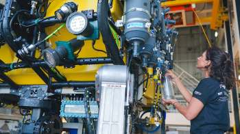 A woman inspects equipment on a yellow underwater vehicle in a technical workshop.