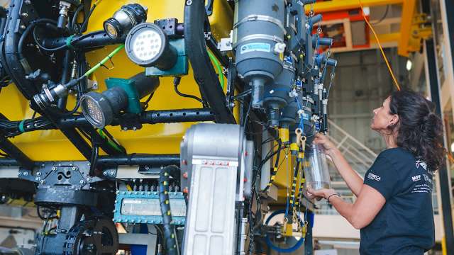 A woman inspects equipment on a yellow underwater vehicle in a technical workshop.