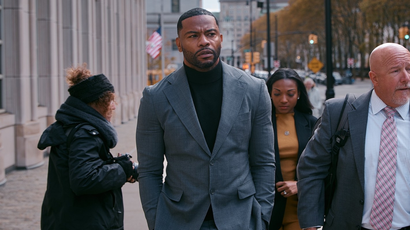 A group of four people, including a man in a suit and three others, walking on a city street.