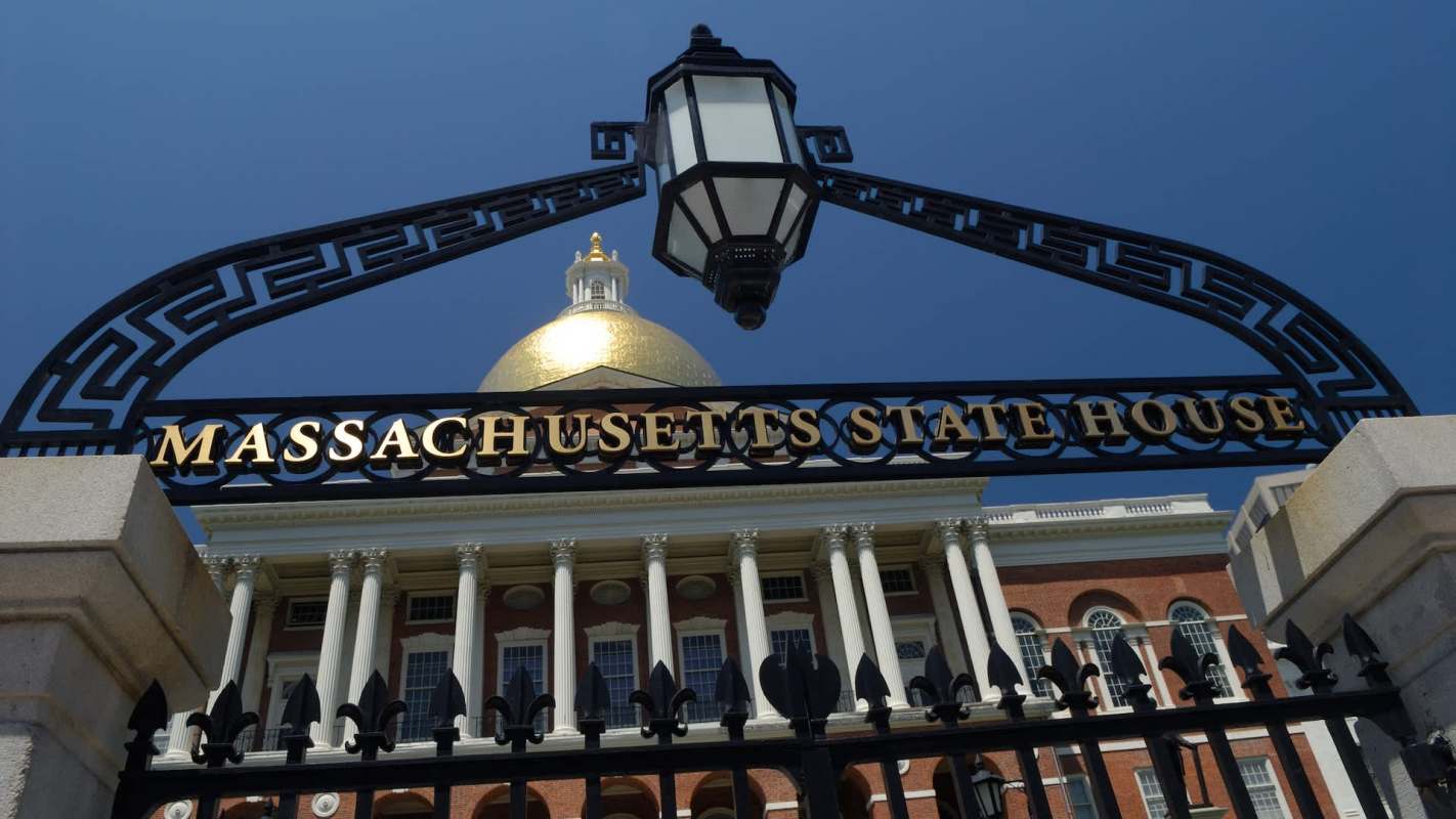 The Massachusetts State House entrance, featuring an ornate black gate with gold lettering.