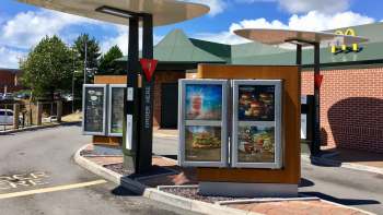 A McDonald's drive-thru with signage and menu boards under a clear blue sky.