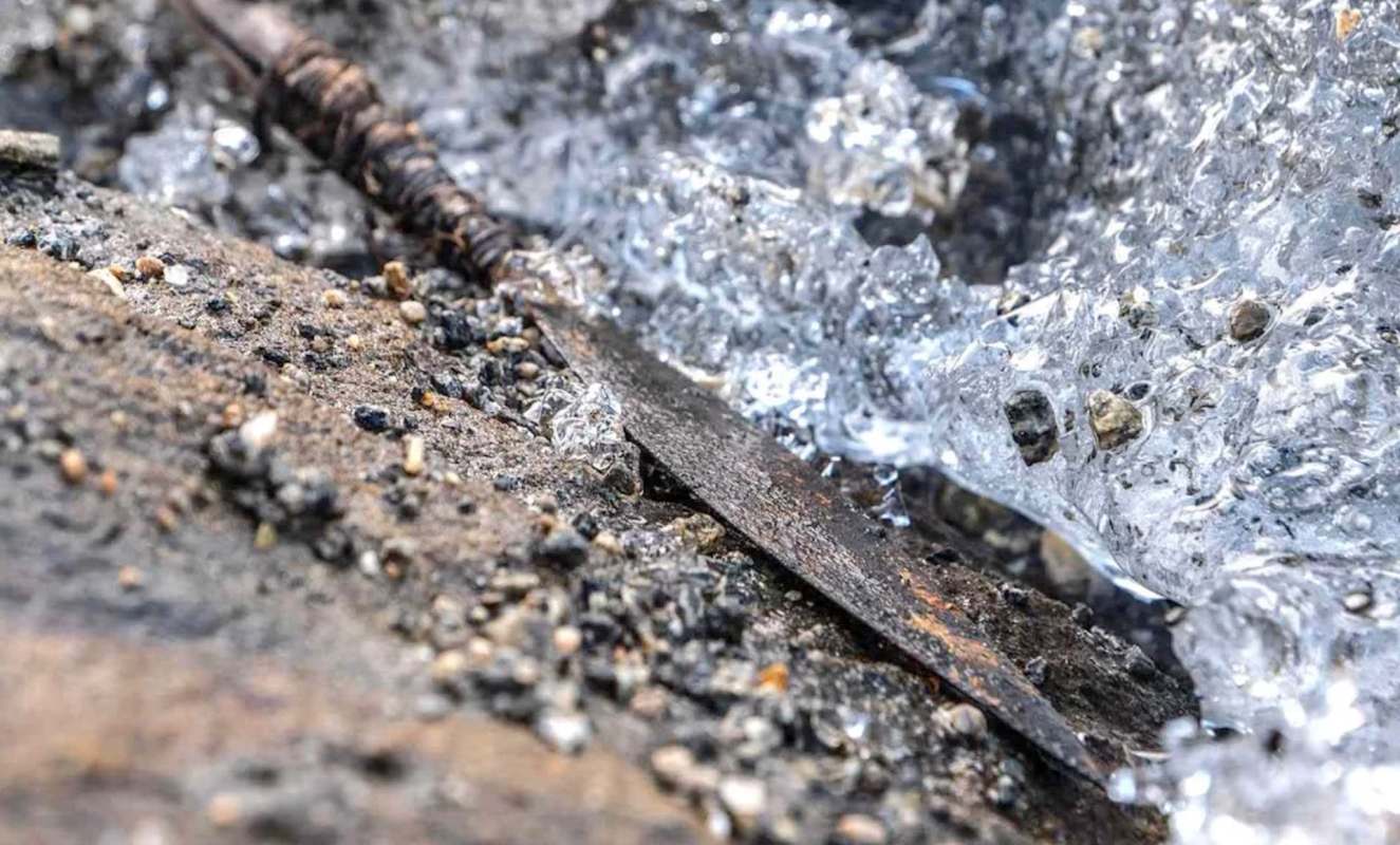 A rusted spearhead surrounded by shallow ice and pebbles.