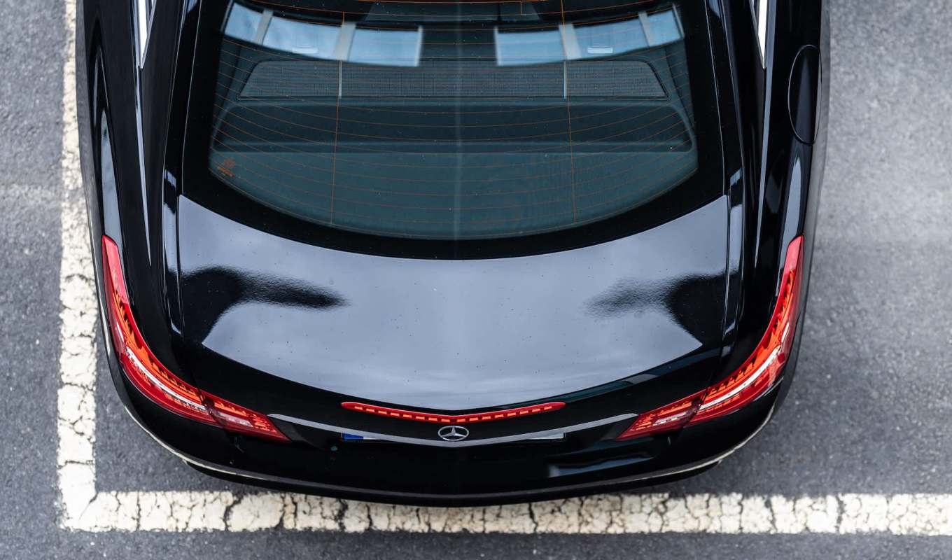 An overhead view of a black luxury Mercedes-Benz with a shiny roof and red taillights, parked in a lot.