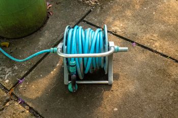 A blue garden hose neatly coiled on a metal reel, positioned on a stone patio.