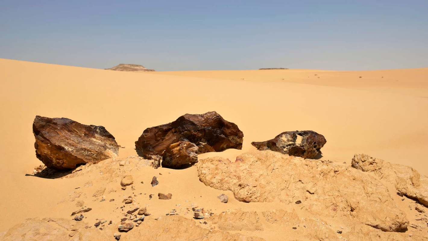 Three large meteorite fragments on a sandy desert landscape under a clear blue sky.