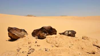 Three large meteorite fragments on a sandy desert landscape under a clear blue sky.