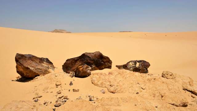 Three large meteorite fragments on a sandy desert landscape under a clear blue sky.