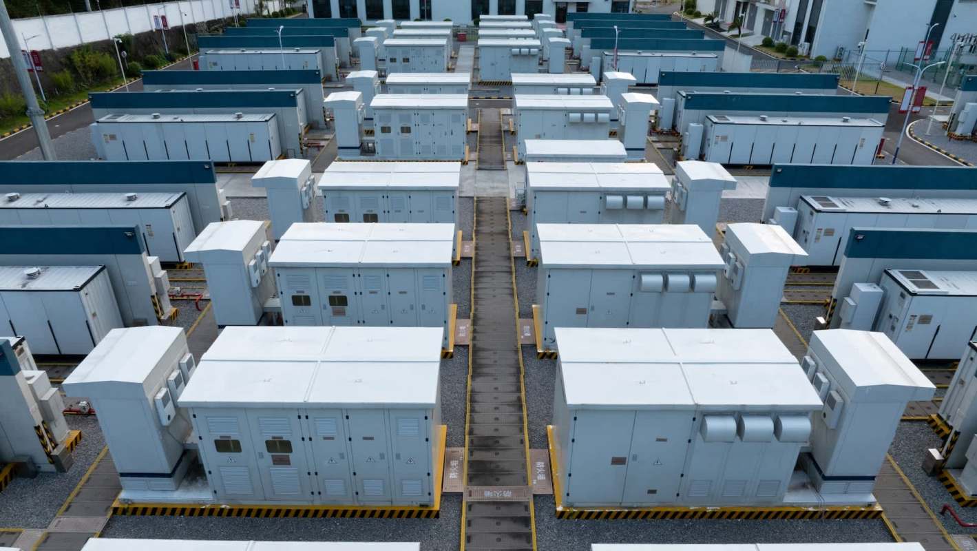 Rows of battery energy storage containers over a gravel surface.