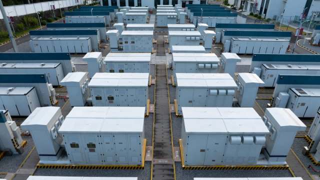 Rows of battery energy storage containers over a gravel surface.