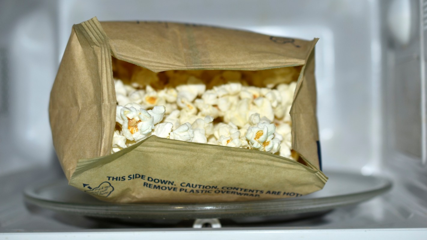 A partially opened bag of popcorn inside a microwave, revealing fluffy popped kernels.
