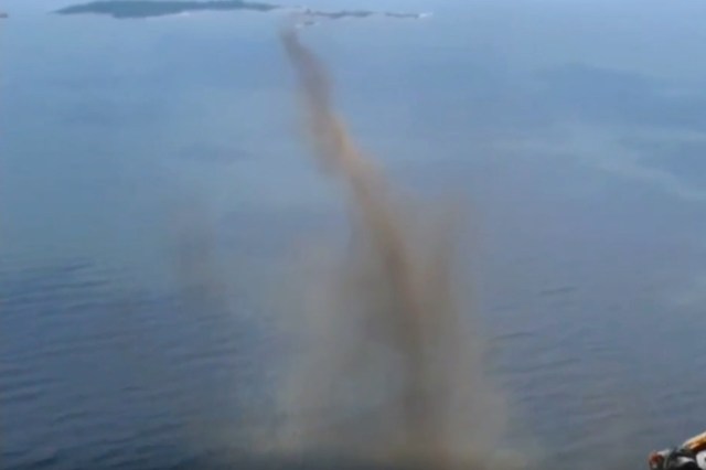 A column of midges rises from the water's surface, appearing like a funnel of smoke.