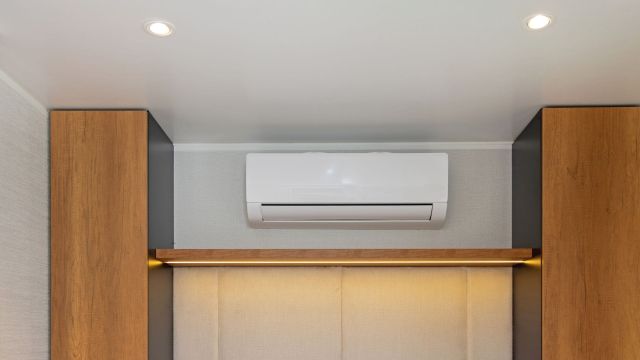 A wall-mounted air conditioner installed above a wooden shelf.