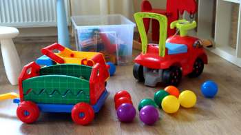 A colorful array of plastic toy vehicles, carts, and balls scattered across a wooden floor.