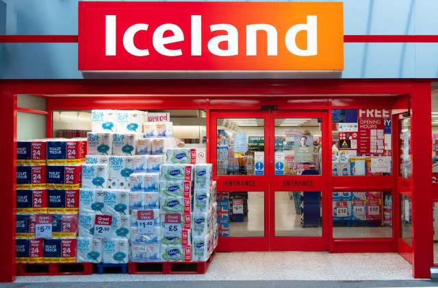 An Iceland store entrance featuring stacks of toilet paper and kitchen rolls outside.