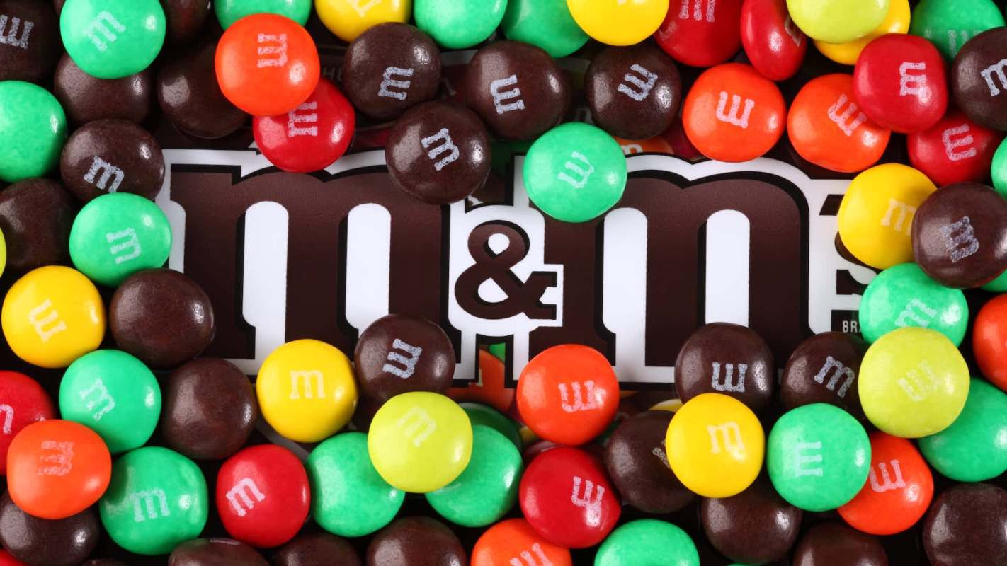 An assortment of M&M's scattered over a partially visible M&M's logo.