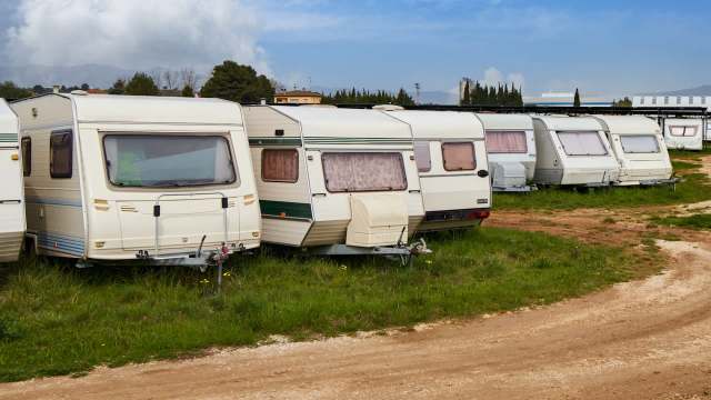 A row of parked caravans on a grassy area beside a dirt path under a partly cloudy sky.