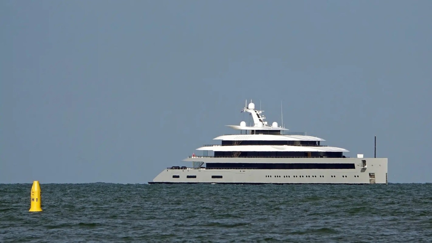 A large luxury yacht sails across calm waters under a clear blue sky.