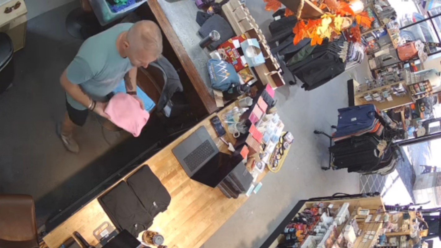 A man in a blue shirt holds a pink item while standing at a checkout counter in a retail store.