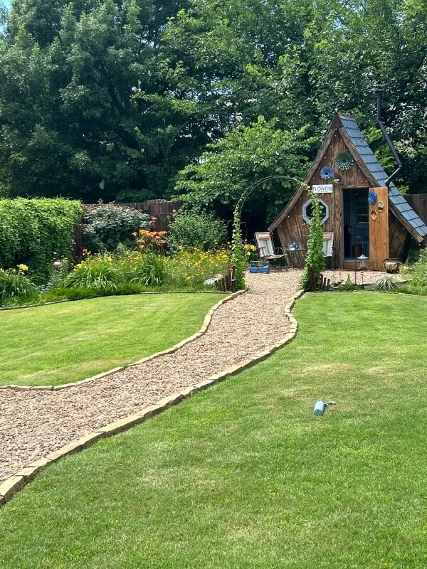 A path leading to a whimsical shed surrounded by flowers and native plants.