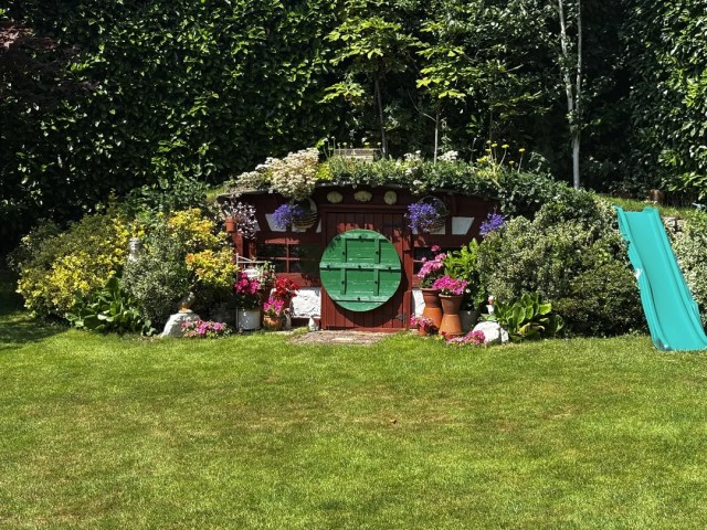 A Hobbit-sized playhouse nestled under greenery and flanked by flowers.